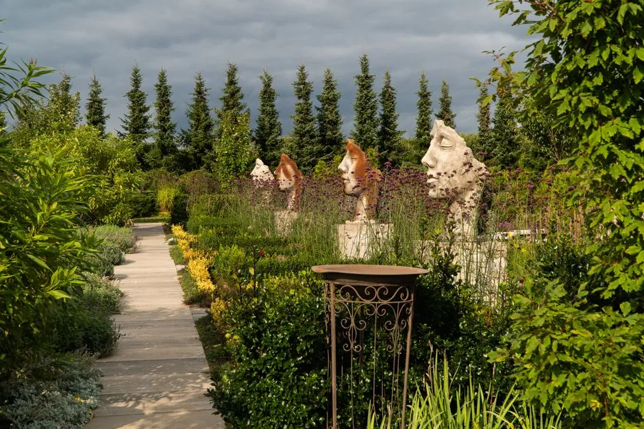 Allee de jardin contemporain, cypres et roses de papier au crepuscule.