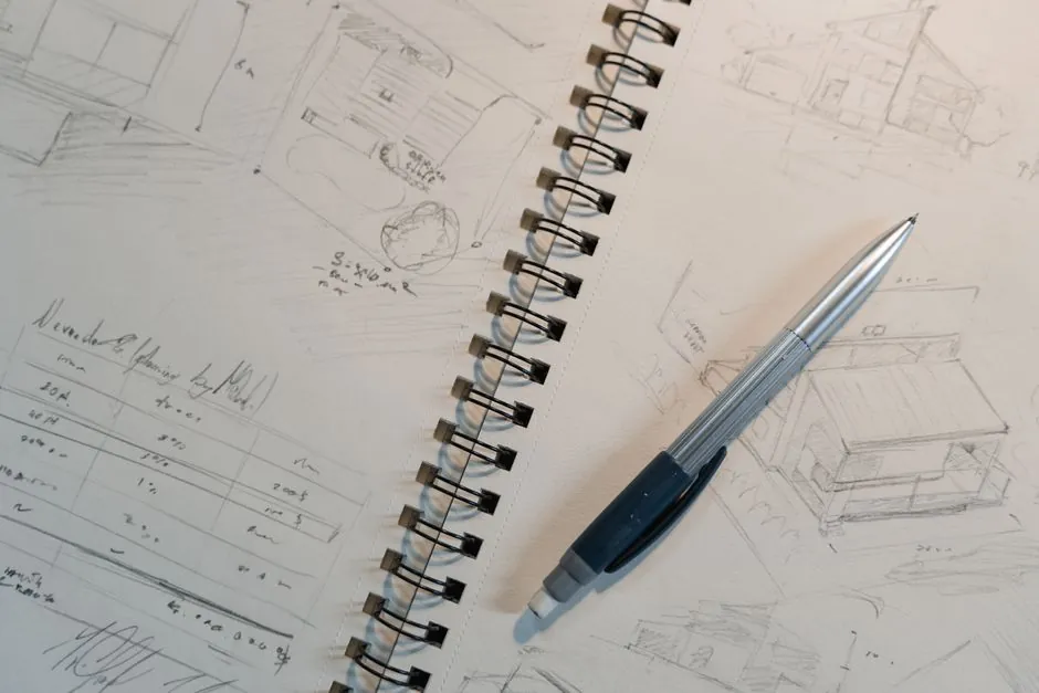 Carnet d'esquisses, plans crayonnes et stylo sur une table d'atelier.